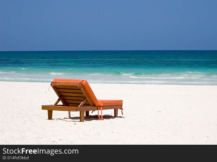 An orange bedchair facing the turquoise sea on a white sand beach in Mexico. An orange bedchair facing the turquoise sea on a white sand beach in Mexico