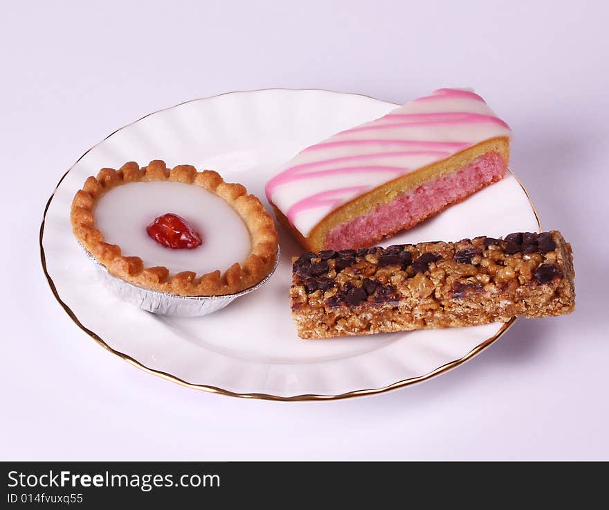 A gilded plate with a selection of cakes, bakewell tart, angel slice and chocolate chip bar. A gilded plate with a selection of cakes, bakewell tart, angel slice and chocolate chip bar