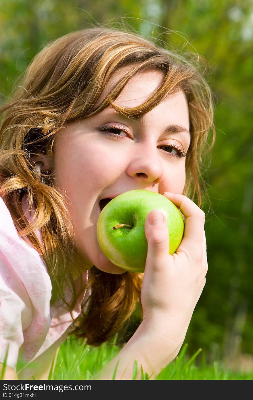 Pretty woman eating green apple on the summer glade