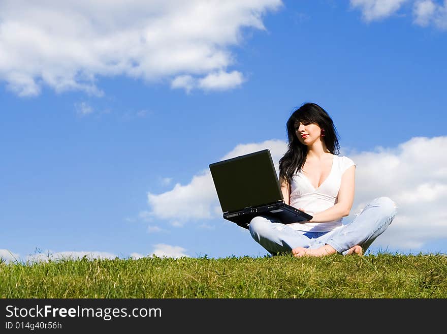 Pretty woman with laptop on the green grass