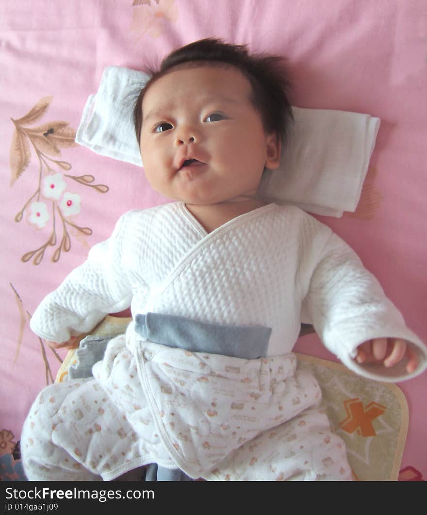 A Chinese infant is smiling on a bed. A Chinese infant is smiling on a bed