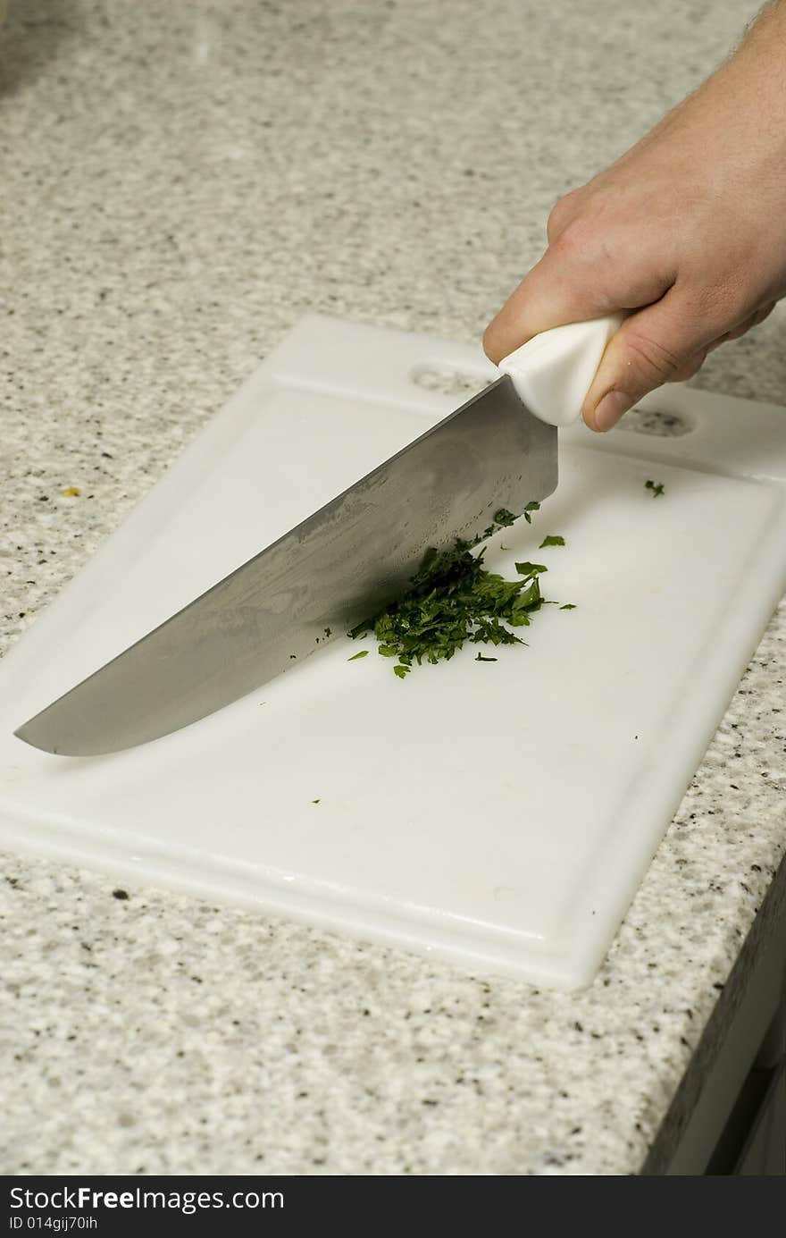 Chef's hands slicing parsley with a knife on a cutting board on a counter top. Vertically framed photo.