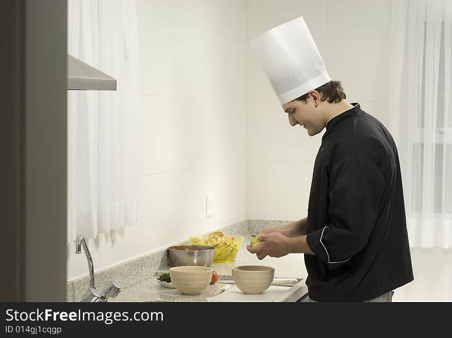 Young, smiling, chef  peeling potatoes into a bowl on a counter next to a bowl and tomatoes. Horizontally framed photo. Young, smiling, chef  peeling potatoes into a bowl on a counter next to a bowl and tomatoes. Horizontally framed photo.