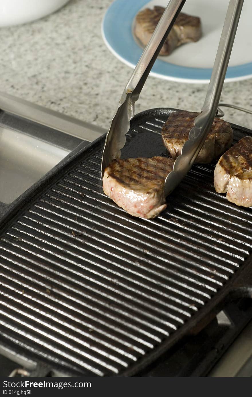 Three steaks on a grill with tongs picking them up. Vertically framed photo.