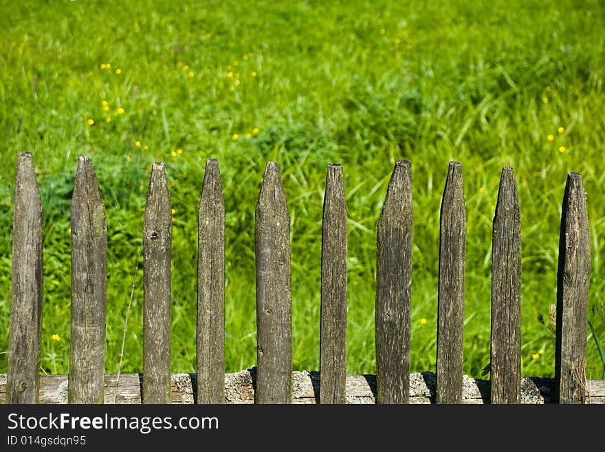 Old wooden fence and a green meadow in a village. Old wooden fence and a green meadow in a village.