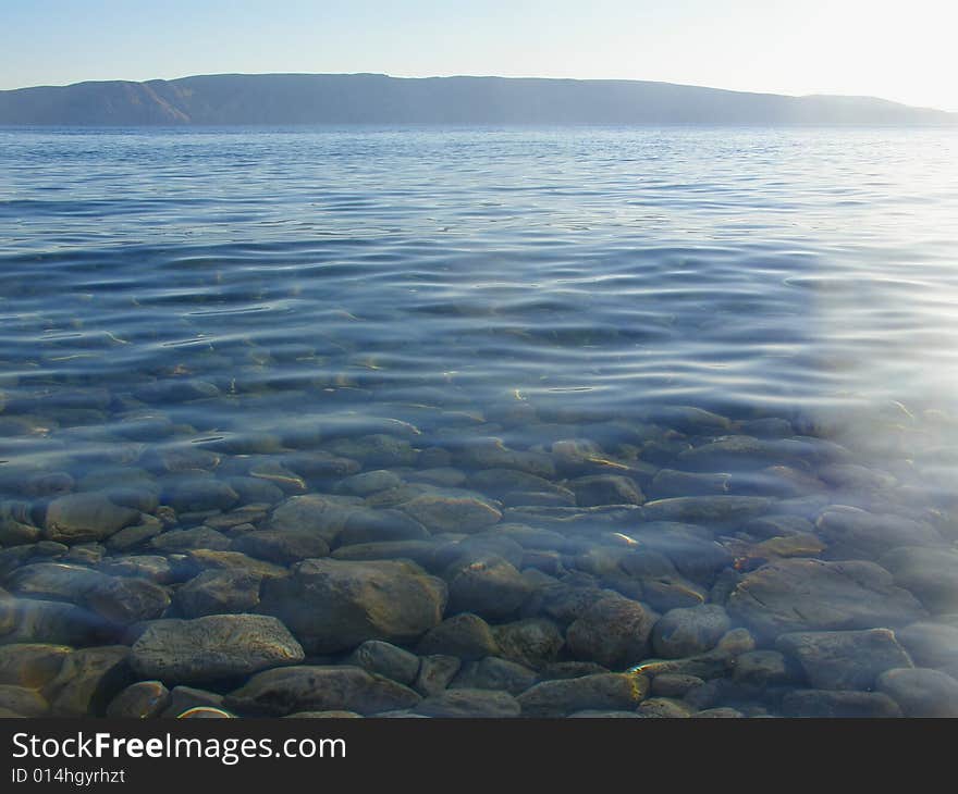 Sibinj - Croatia postcard: Transparent sea water with pebbles, Krk island in the background. Sibinj - Croatia postcard: Transparent sea water with pebbles, Krk island in the background