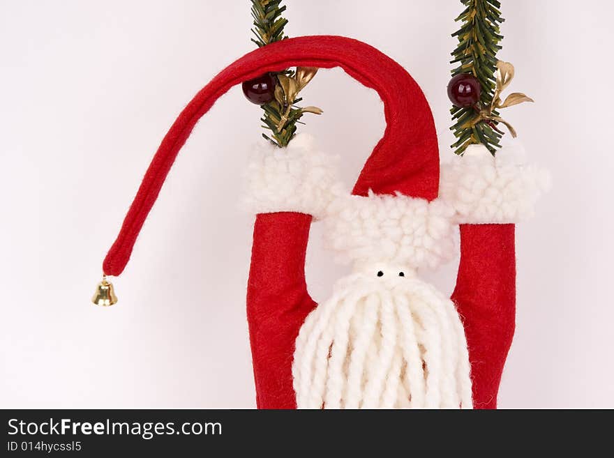 A felt and yarn folk art Santa with a bell topped red hat swings from strands of evergreen.