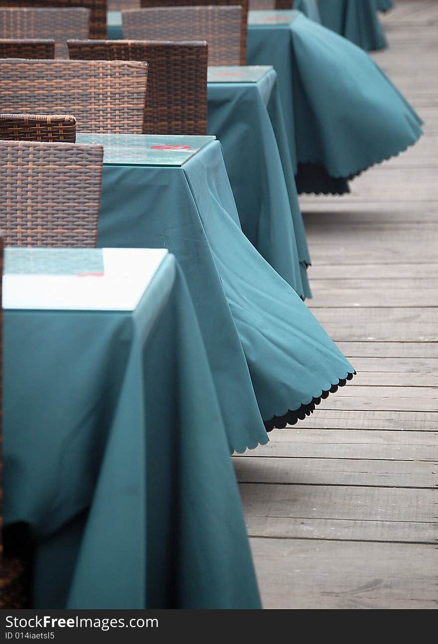 Table and chairs on wooden floor in a outdoor bar at the beach. Table clothes waving in the wind.