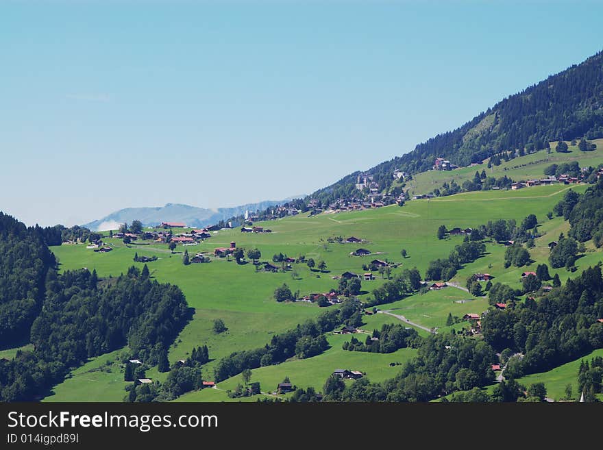 Summer rural landscape view on green Alps mountains, trees, slopes, and detached houses under clear sky. Alps, Switzerland, europe. Summer rural landscape view on green Alps mountains, trees, slopes, and detached houses under clear sky. Alps, Switzerland, europe.