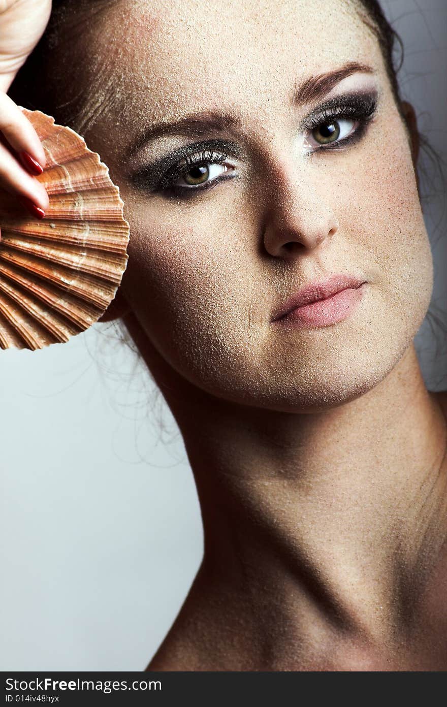 Beauty portrait of a young beautiful woman with sand on her skin and a shell. Beauty portrait of a young beautiful woman with sand on her skin and a shell