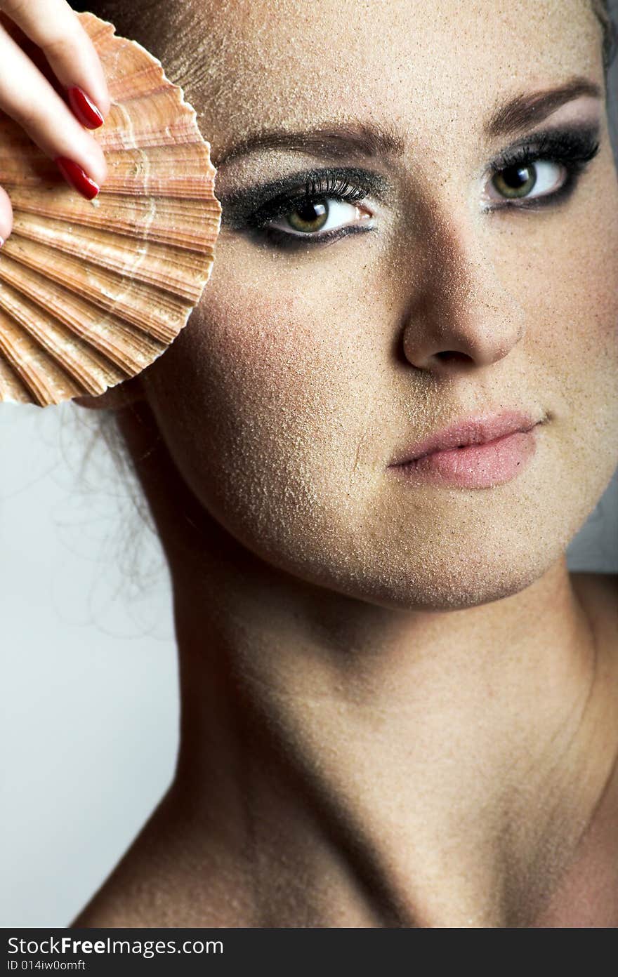 Beauty portrait of a young beautiful woman with sand on her skin and a shell. Beauty portrait of a young beautiful woman with sand on her skin and a shell