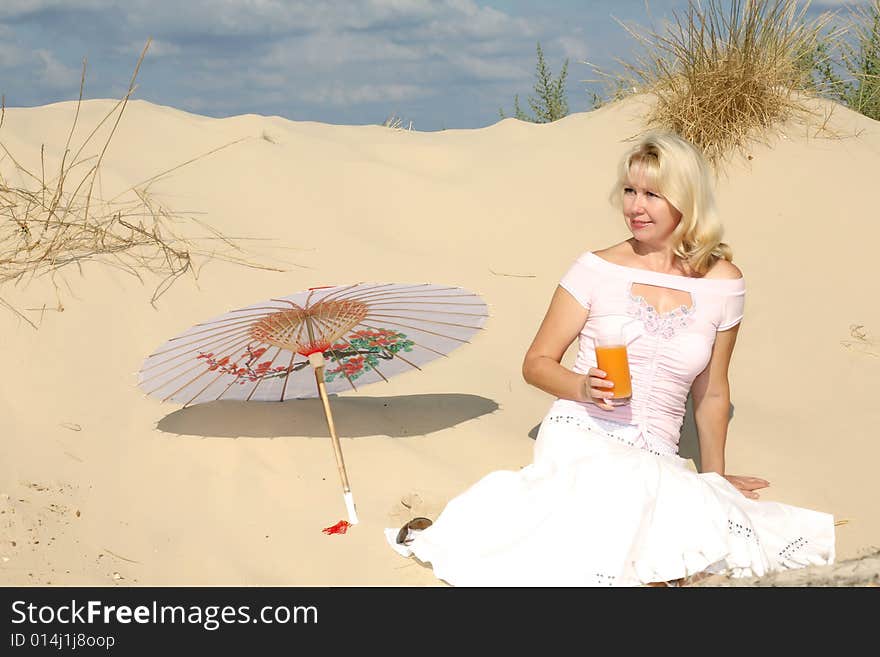 A young woman sits on sand with glass of juice and umbrella. A young woman sits on sand with glass of juice and umbrella