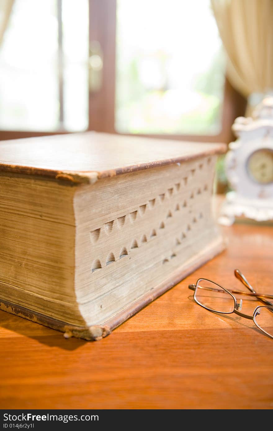 An antique reference book with eyeglasses and an old clock.