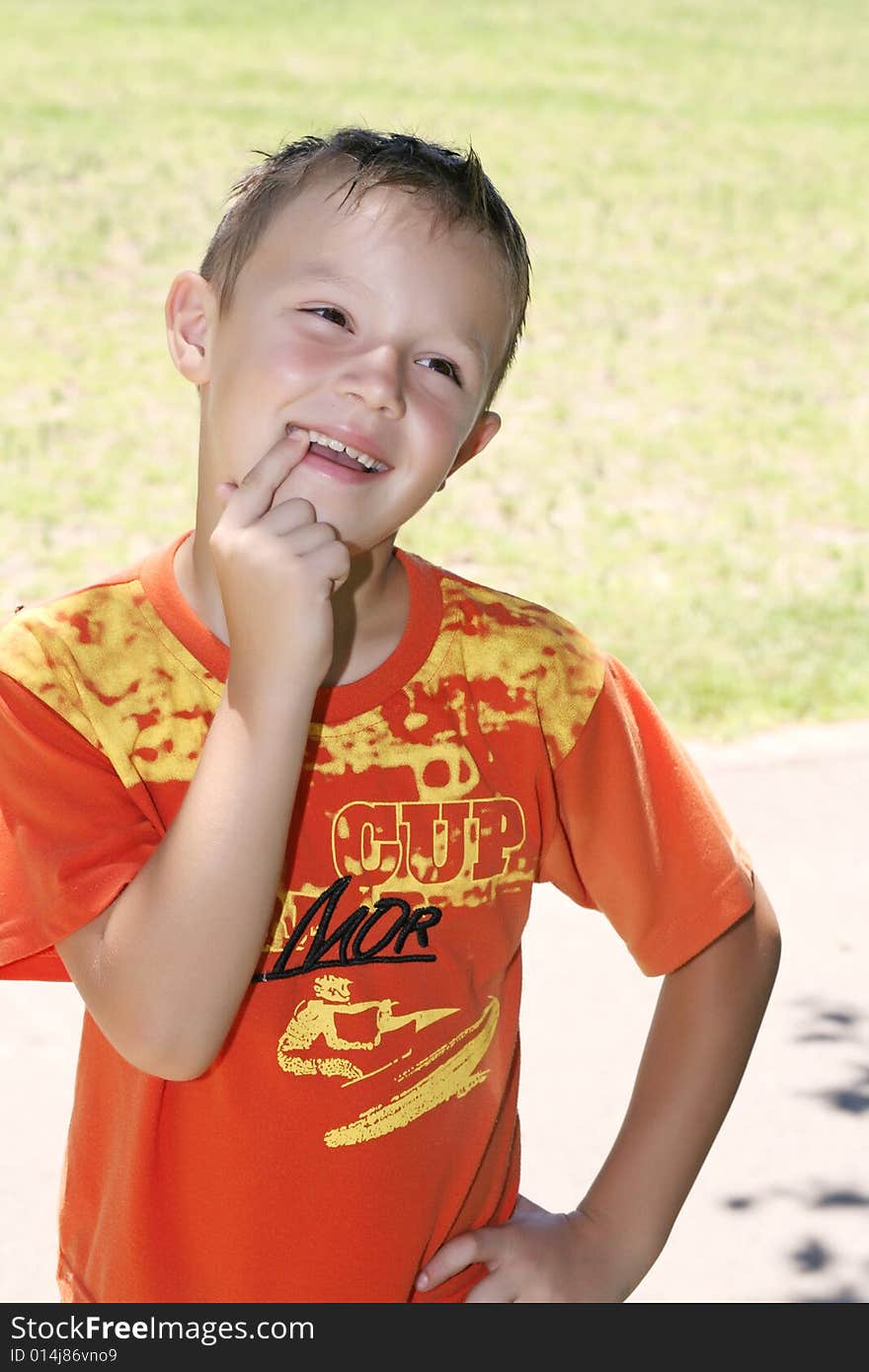 A little boy in an orange sport shirt shows a finger on the healthy teeth