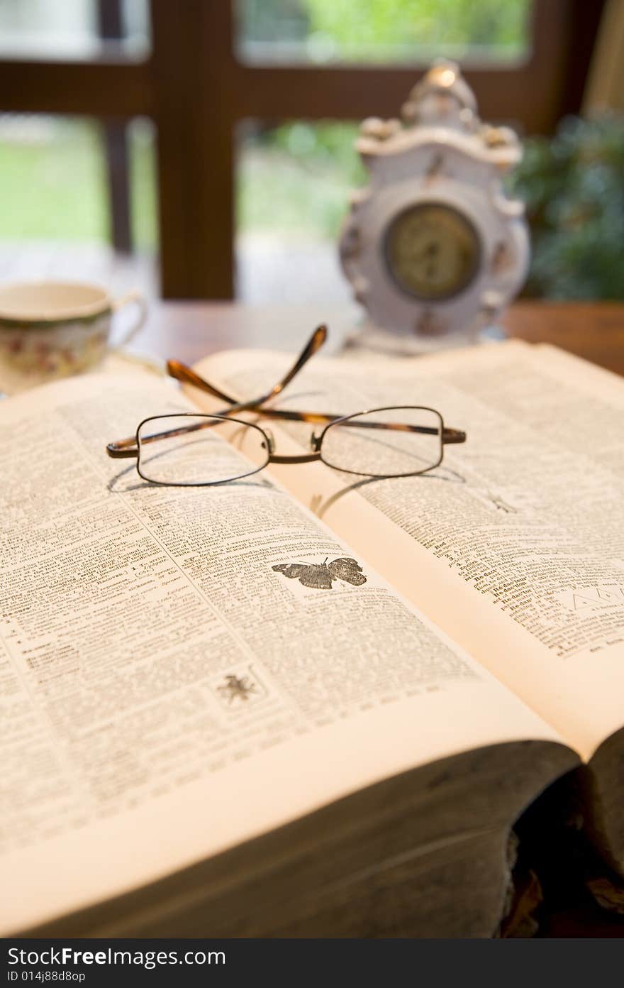 An antique reference book with eyeglasses and an old clock.