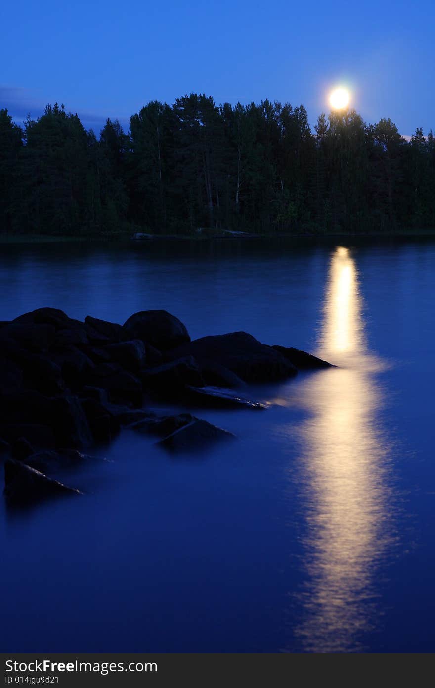 Moon rising and reflecting in the still water of a lake