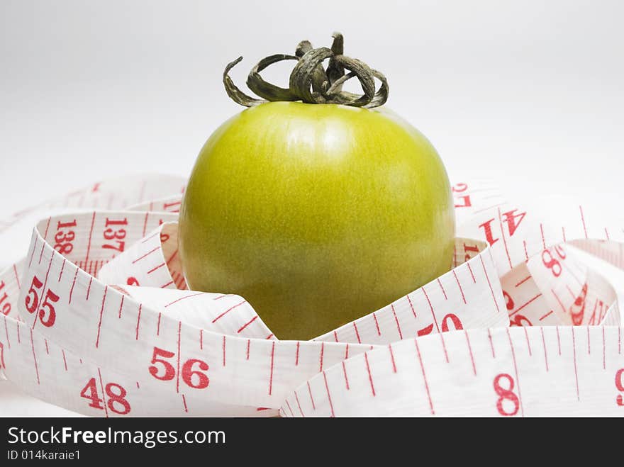 Studio shot of green tomato and measuring tape against white background. Studio shot of green tomato and measuring tape against white background