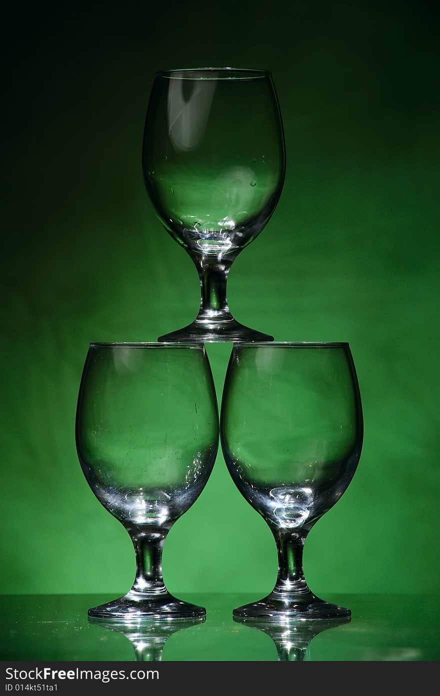 Three wine glasses forming a pyramid, on dark green unregular background, lit from below. Three wine glasses forming a pyramid, on dark green unregular background, lit from below