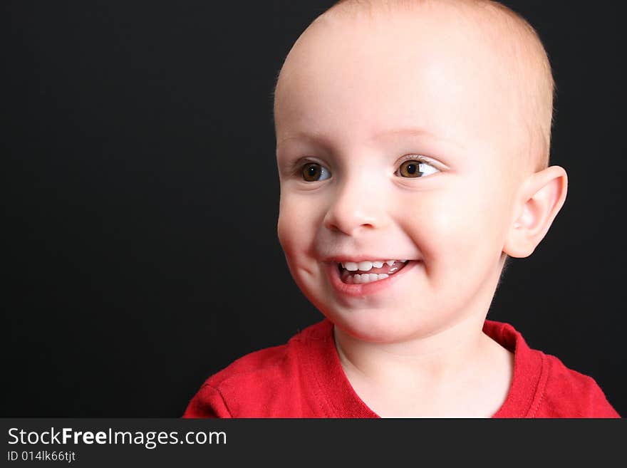 Blonde toddler against a black background with a big smile