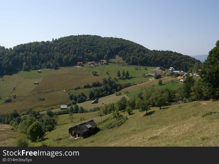 Summer mountainous green glade with small country estate