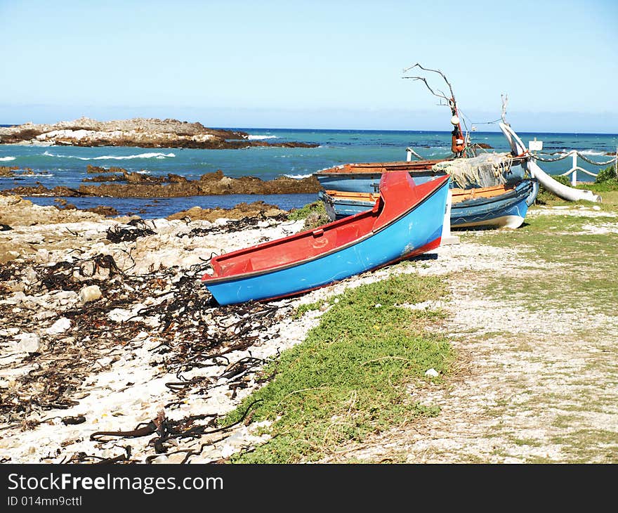 2 old fishing boats on land with a shore covered in bamboo and rocks and the sea in tha background