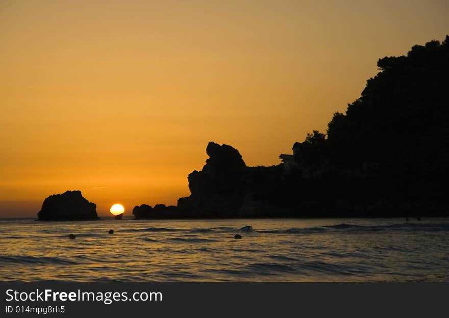 Sunset over Greece seen from Corfu island with rocks in foreground. The sea is the Ionian sea. Sunset over Greece seen from Corfu island with rocks in foreground. The sea is the Ionian sea.