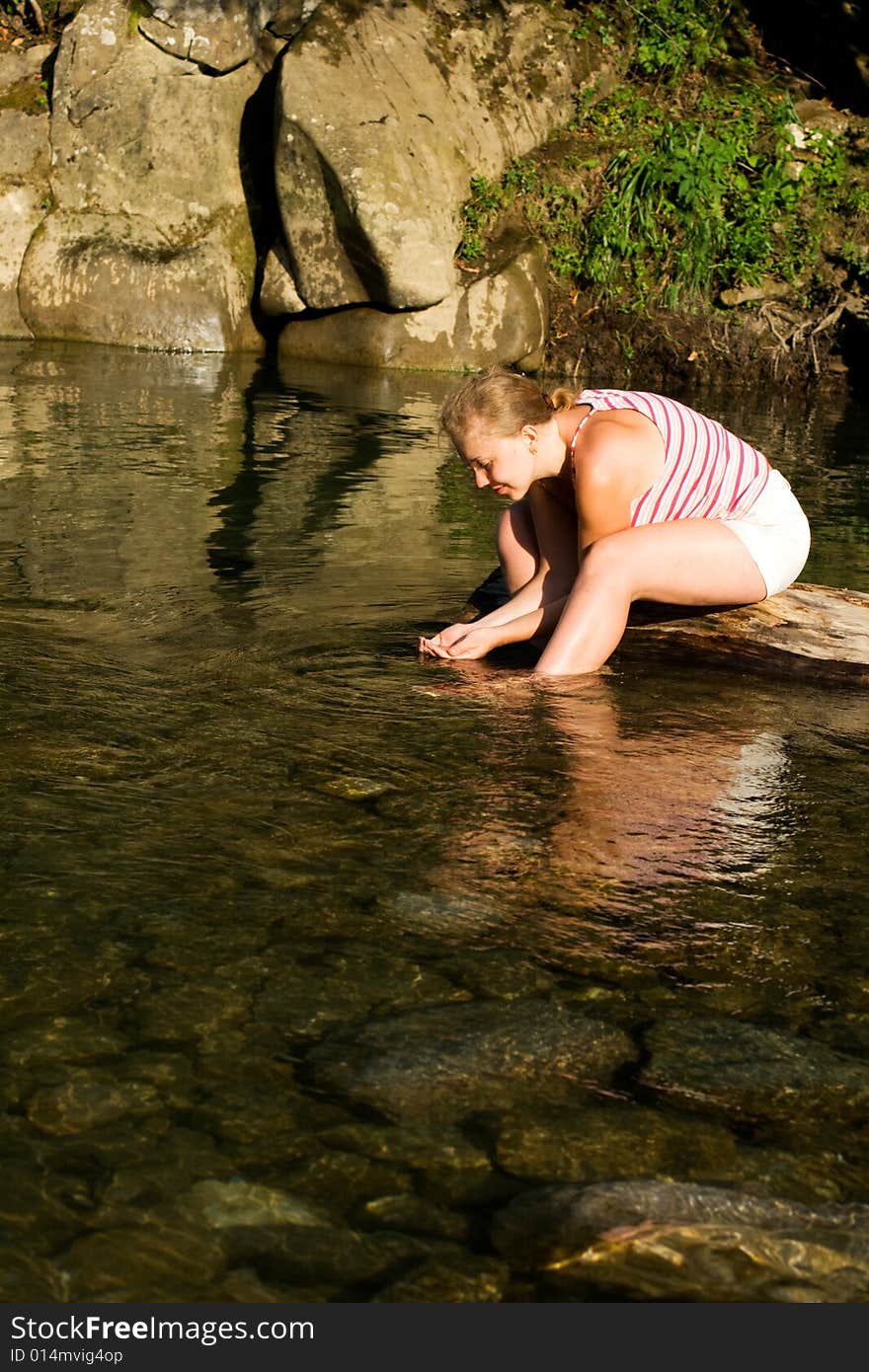 Young woman drinking water in the mountain river