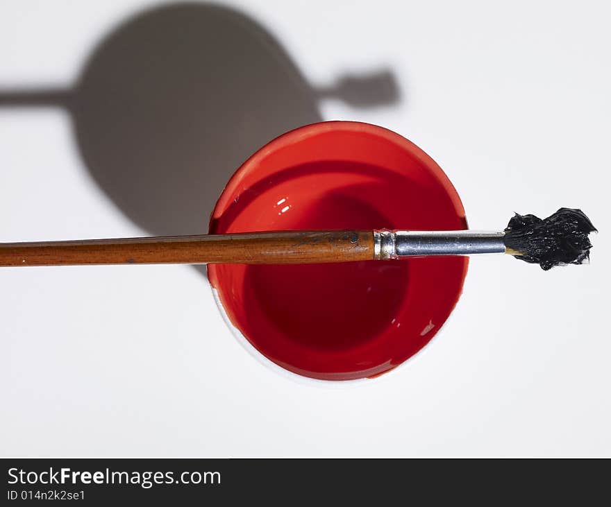 A small round brush loaded with thick black paint rests on top of a styrofoam cup of red paint. A small round brush loaded with thick black paint rests on top of a styrofoam cup of red paint.