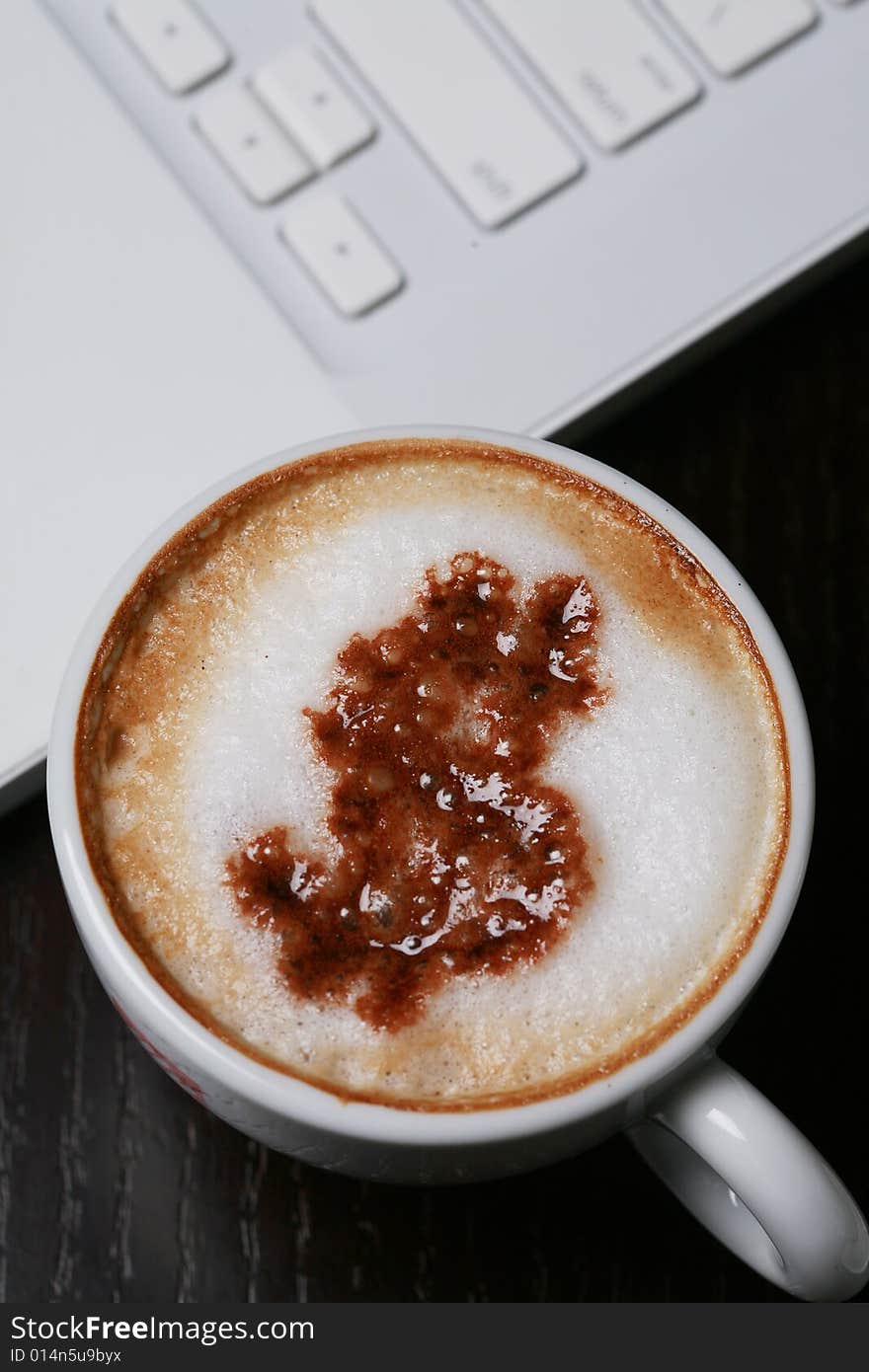 A cup of cappucino with dollar sign on computer's keyboard