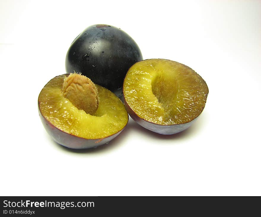 A single plum behind another plum that was cut in half on a white background. A single plum behind another plum that was cut in half on a white background.