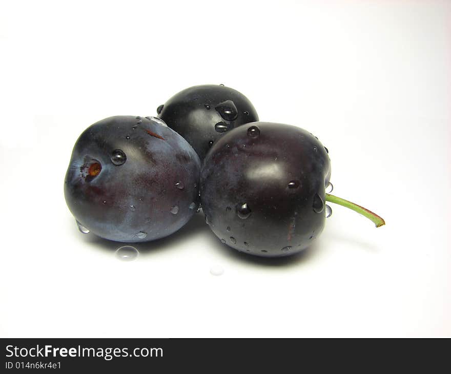 Three plums that were sprayed with water on a white background.