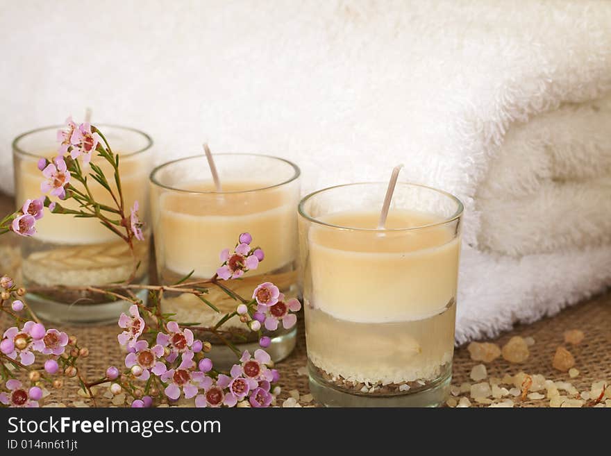 Relaxing spa scene with a white rolled up towel, pink flowers, beautiful handmade candles and bath salts