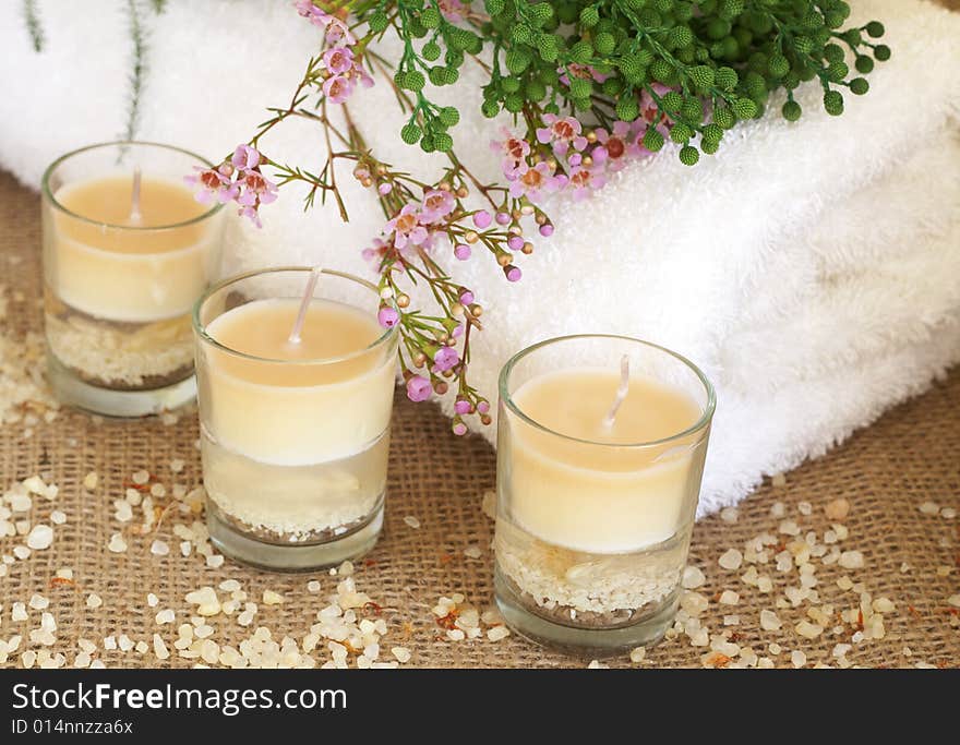 Relaxing spa scene with a white rolled up towel, pink and green flowers, beautiful handmade candles and bath salts