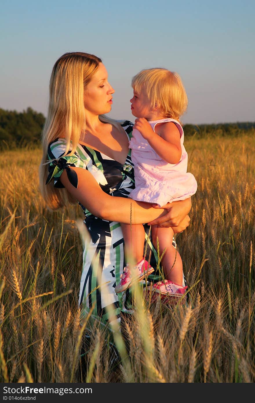 Mother holds child on hands in a wheaten field