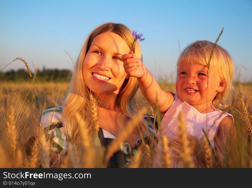 Mother with child sit in wheaten field with cornf