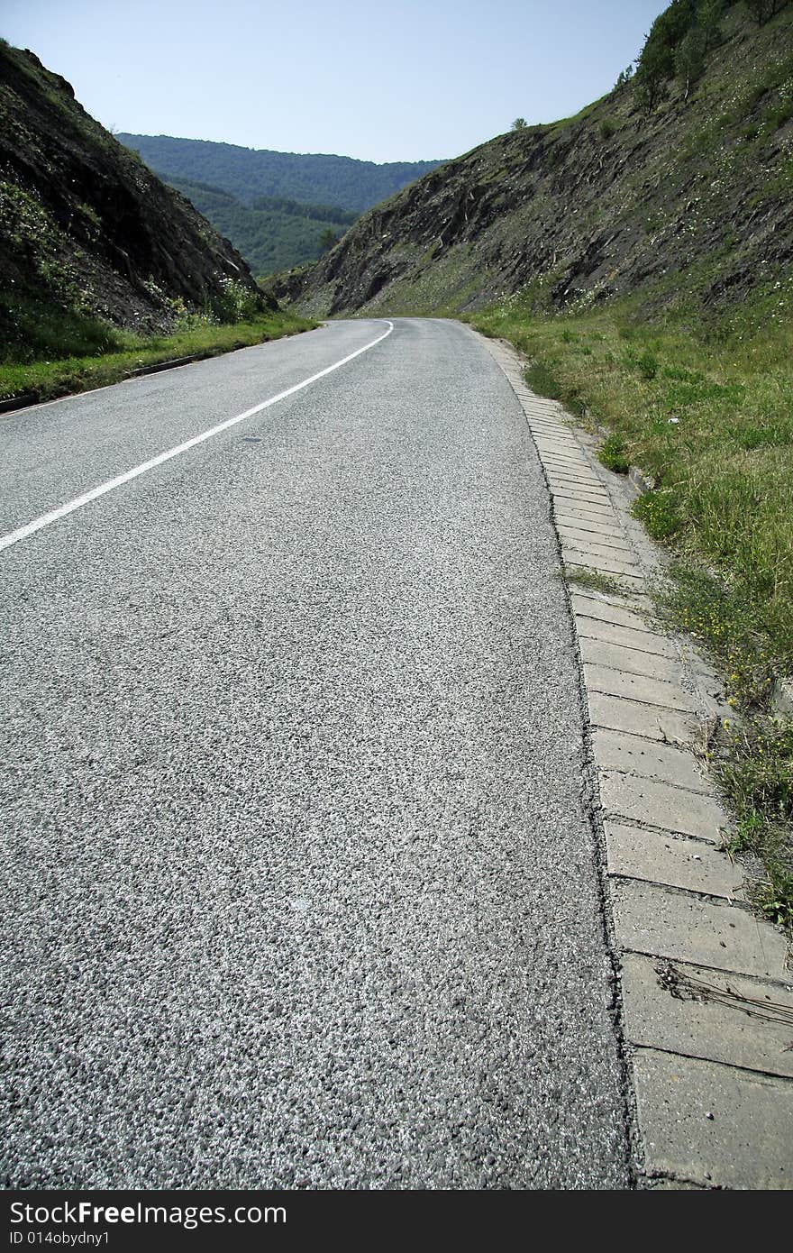 Empty road between two hills, left curve in distance