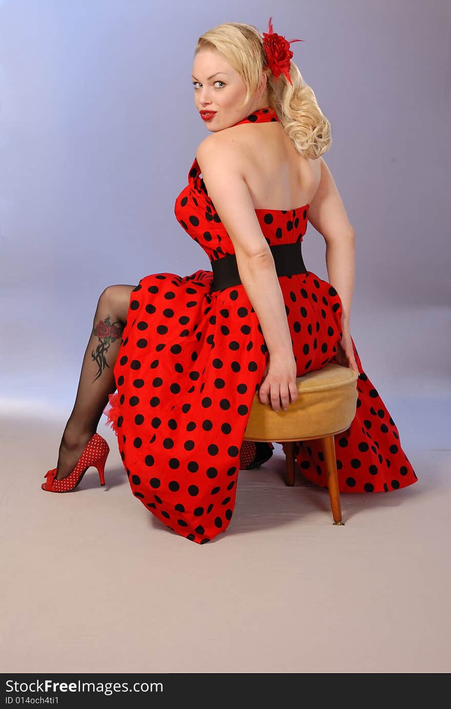 Attractive fifties style pinup blond seated in red polka-dot dress. Attractive fifties style pinup blond seated in red polka-dot dress