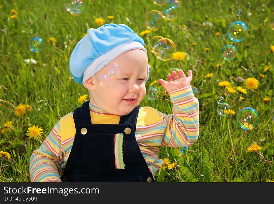 Child sits on grass and looks on soap bubbles