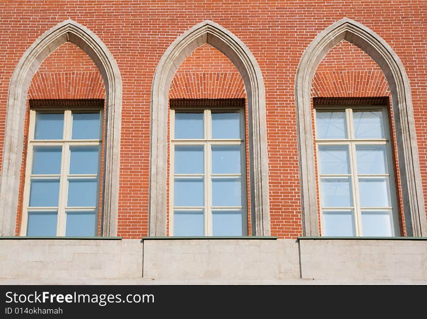 Three high glassed white-framed windows in a red brick wall