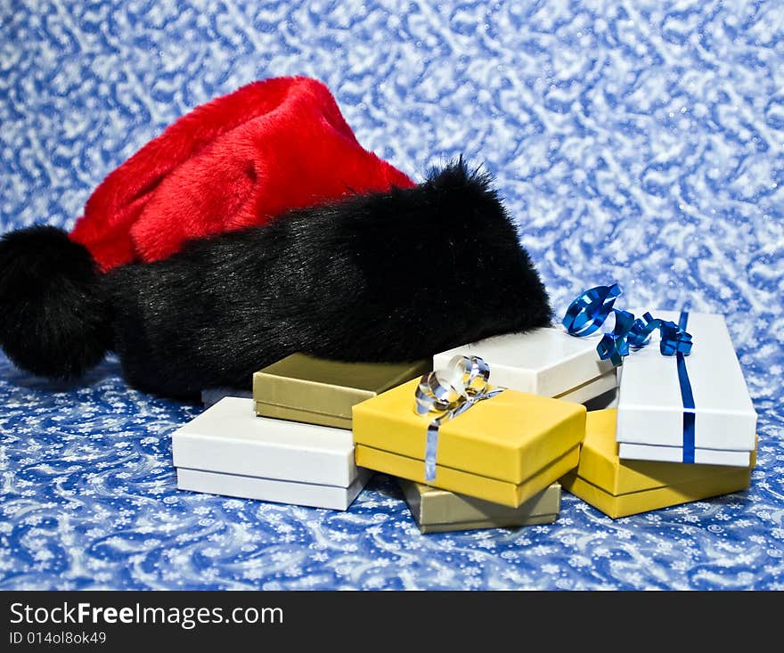 Santa hat with box gifts on a blue winter background. Santa hat with box gifts on a blue winter background.