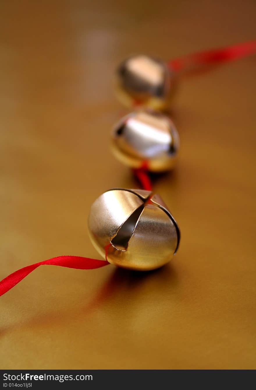 Three gold bells with red ribbon, all on a metallic gold background.