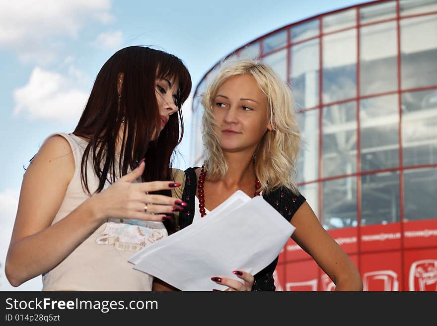 Two young women having a discussion, modern office building on the background.