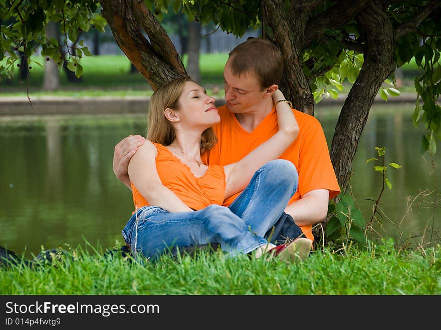 Loving couple kisses under a tree on a river bank