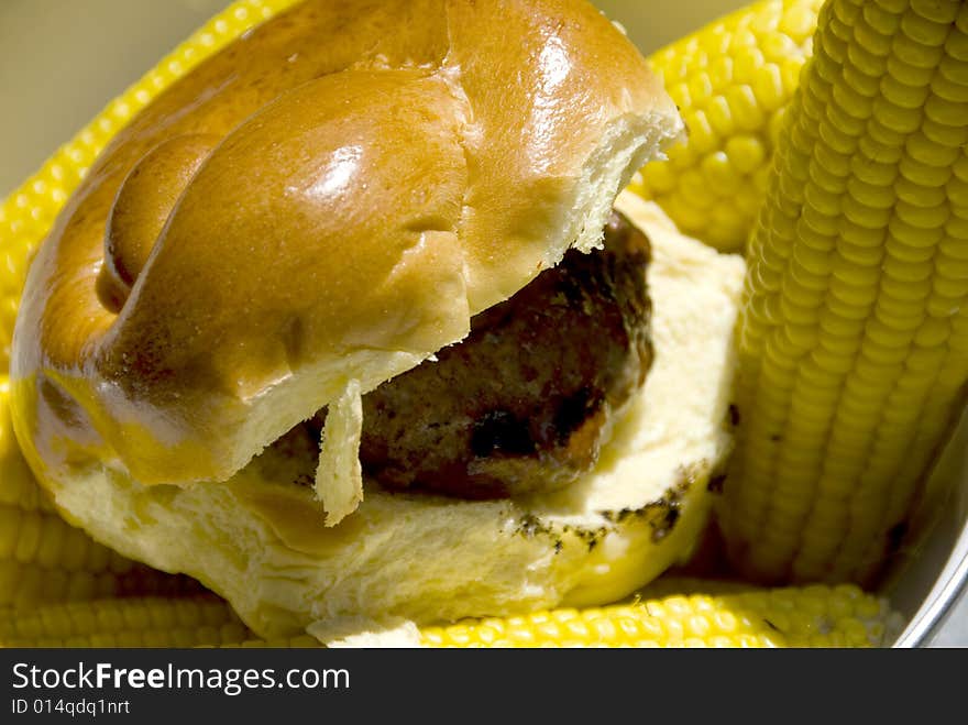 Single hamburger on a greasy bun with corn on the side. Single hamburger on a greasy bun with corn on the side