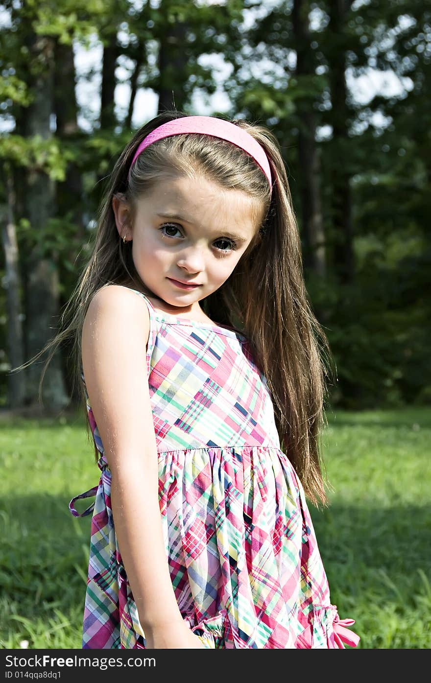 Beautiful Child modeling a plaid sundress in an outdoor setting wearing a pink headband.