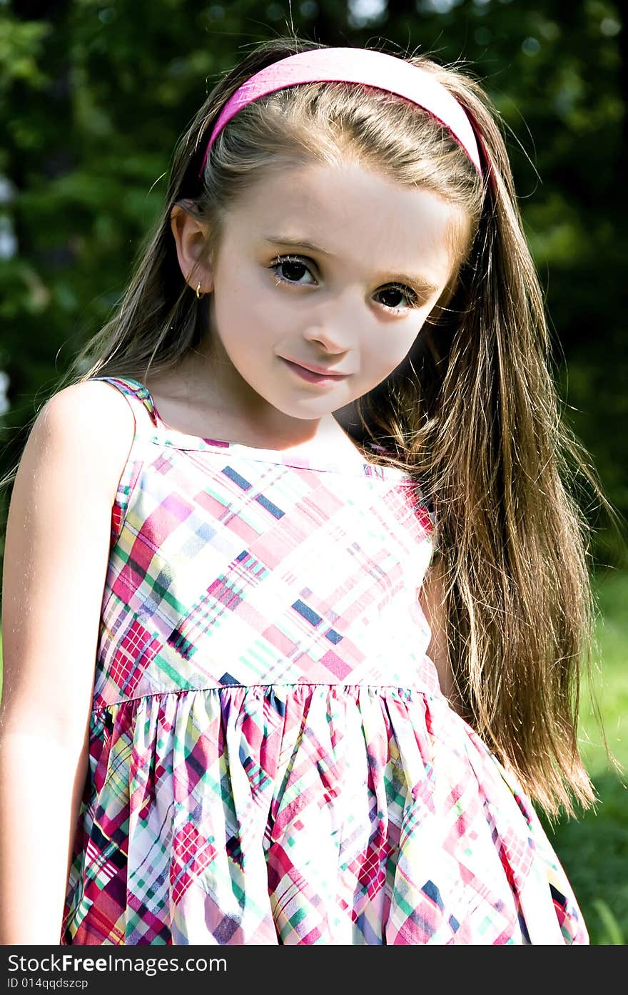 Beautiful little brunette, brown eyed, girl with long hair wearing a plaid dress and pink headband in an outdoor setting. Beautiful little brunette, brown eyed, girl with long hair wearing a plaid dress and pink headband in an outdoor setting.