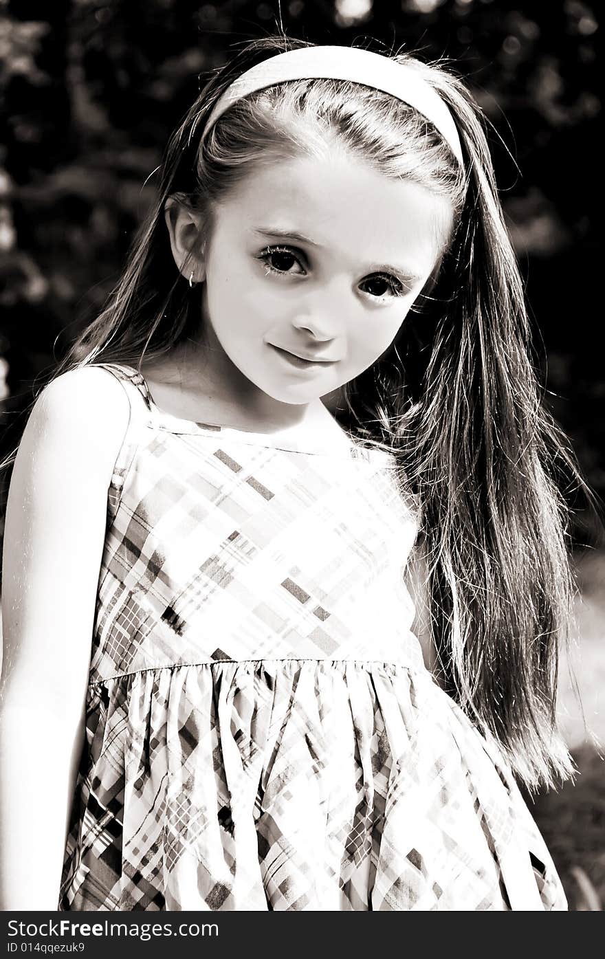 Beautiful little brunette, brown eyed, girl with long hair wearing  a plaid dress and pink headband in an outdoor setting. Beautiful little brunette, brown eyed, girl with long hair wearing  a plaid dress and pink headband in an outdoor setting.