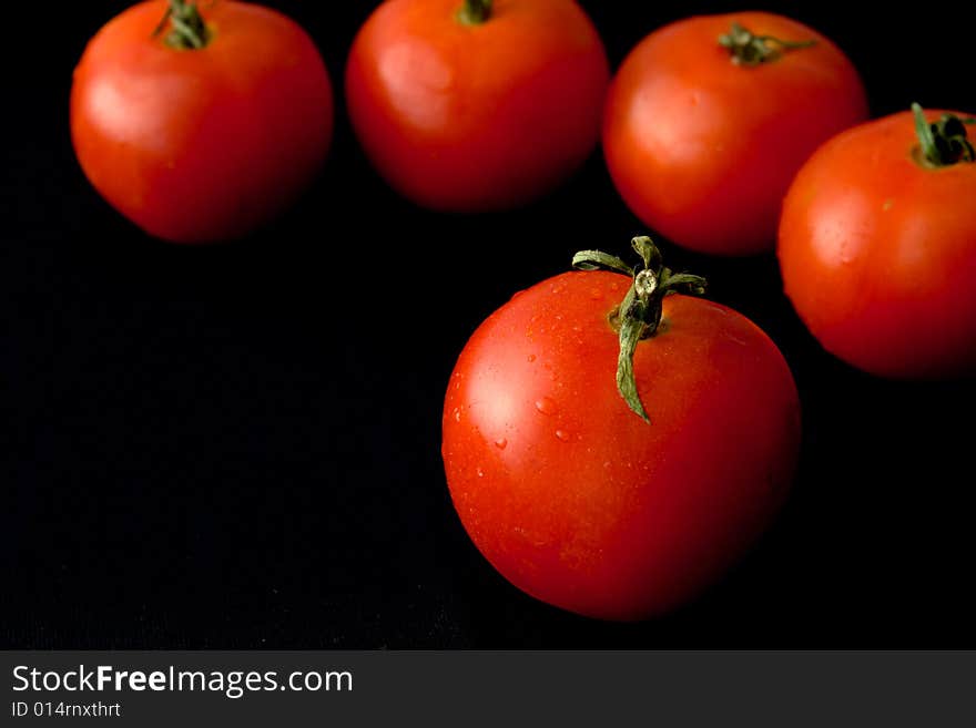 Tomatoes on a black background with drops of water. Even the tomato can look is refined