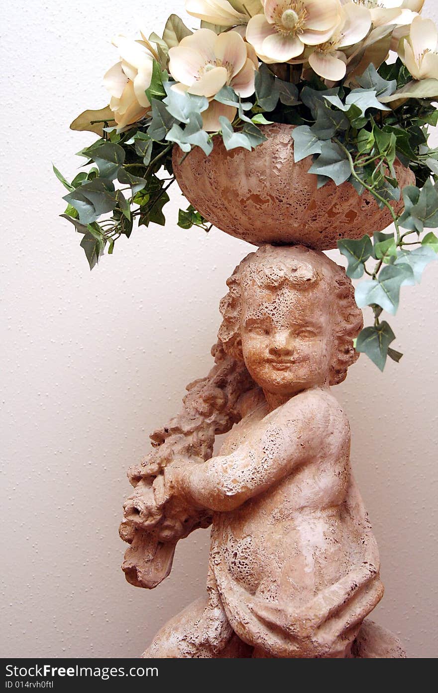 A cherub statue holds flowers on top of its head. A cherub statue holds flowers on top of its head.