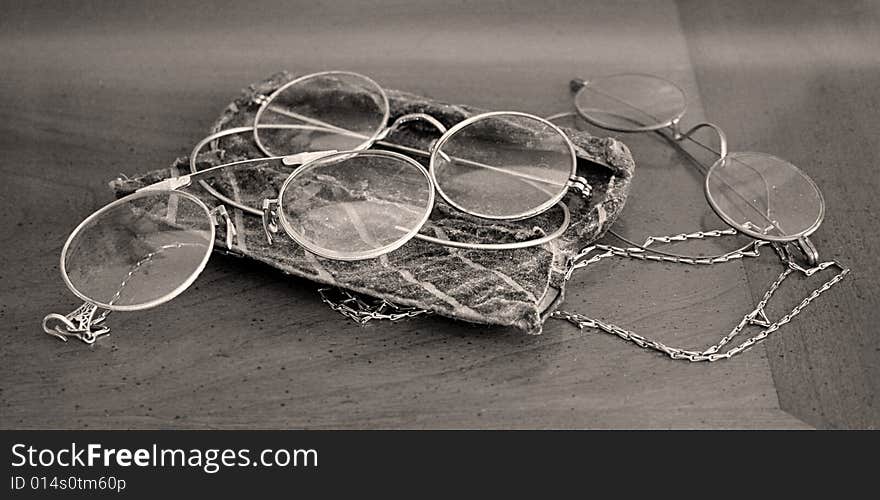 Three pair of antique glasses sit on a wooden table in black and white.